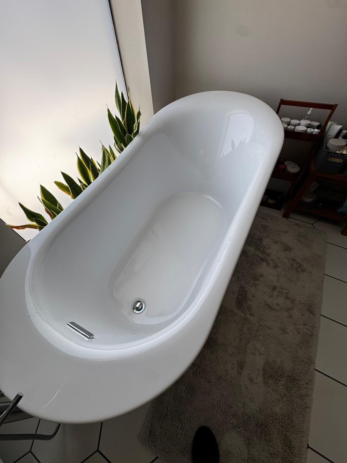 White freestanding bathtub in a modern bathroom beside a plant and rug