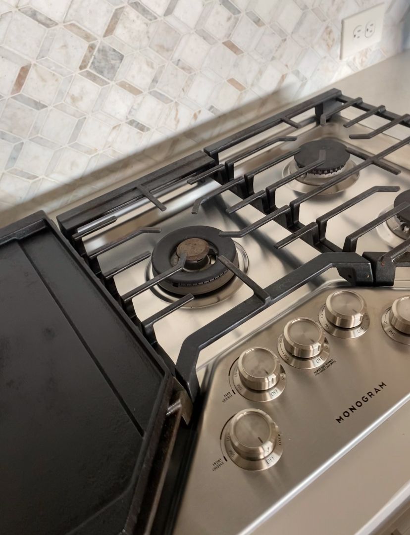 Stainless steel gas stovetop with four burners and control knobs on a white tiled kitchen counter