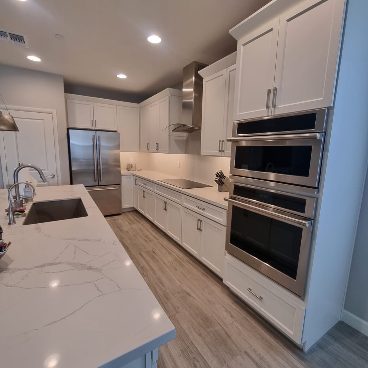 Modern white kitchen with island, stainless steel appliances, and light wood flooring.