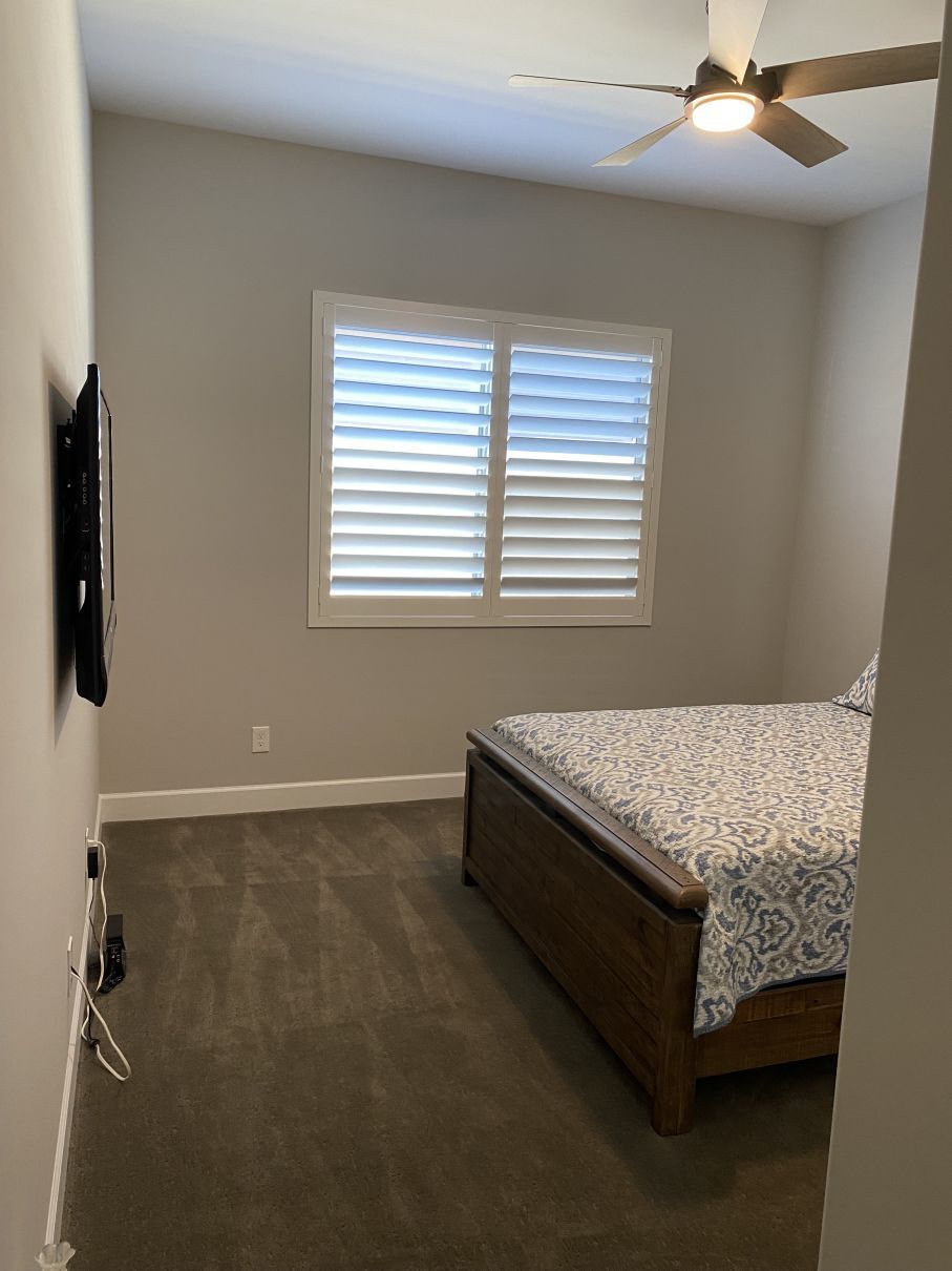 Empty bedroom with gray walls, dark wood floor, window shutters, ceiling fan, and a bed along the right wall