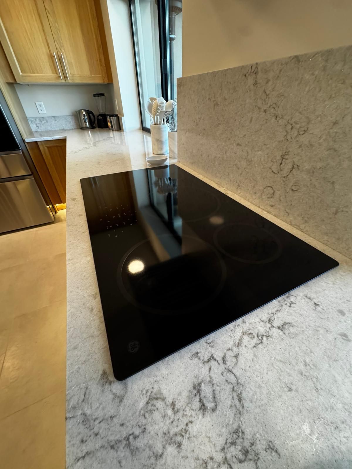 Black glass stovetop on a light marble kitchen countertop, with wood cabinets in the background