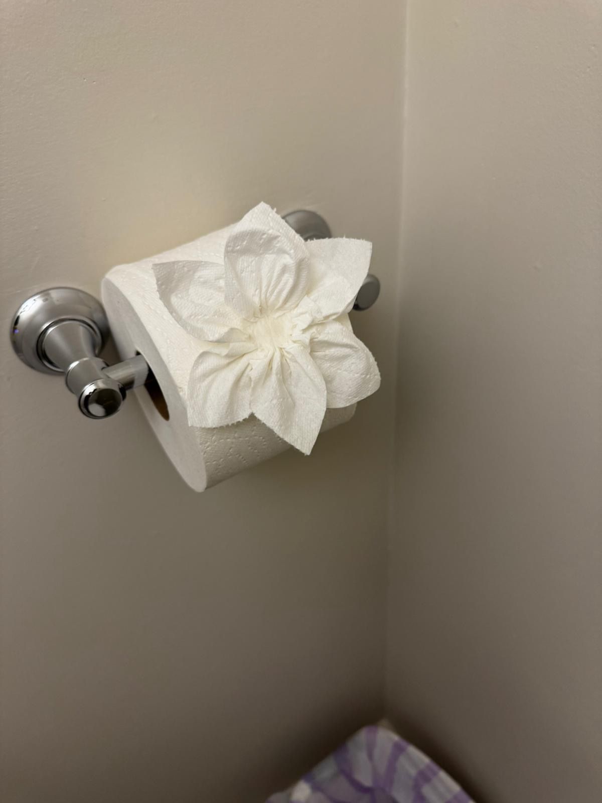 White tissue flower on a chrome toilet paper holder in a beige bathroom corner