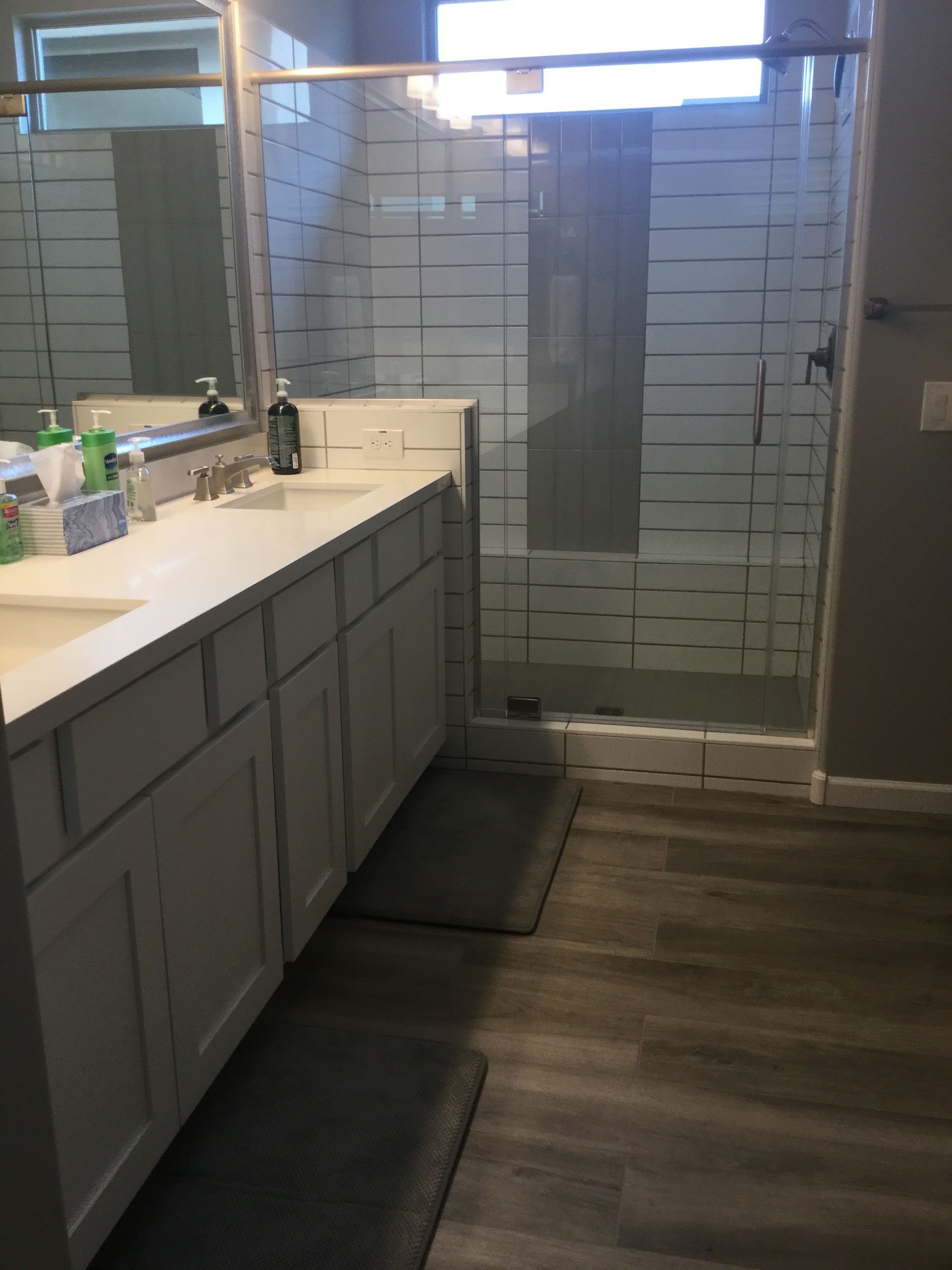 Bathroom with white vanity, sink, mirror, and glass-enclosed shower over dark wood flooring.