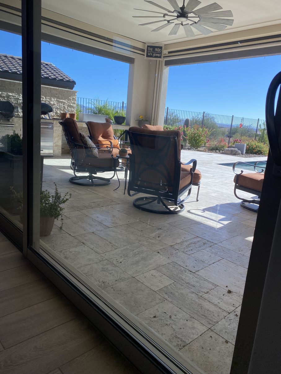 Covered patio with outdoor chairs, ceiling fan, and ocean view through open sliding doors