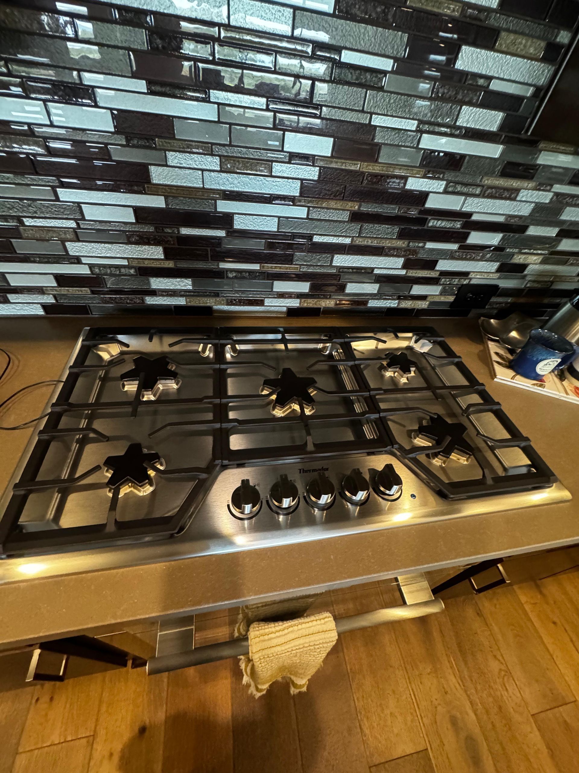 Stainless steel gas stovetop with four burners on a wooden counter, under a mirrored backsplash.