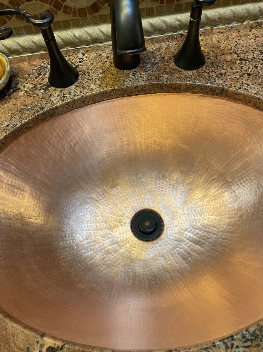 Copper bathroom sink with dark faucet and granite countertop