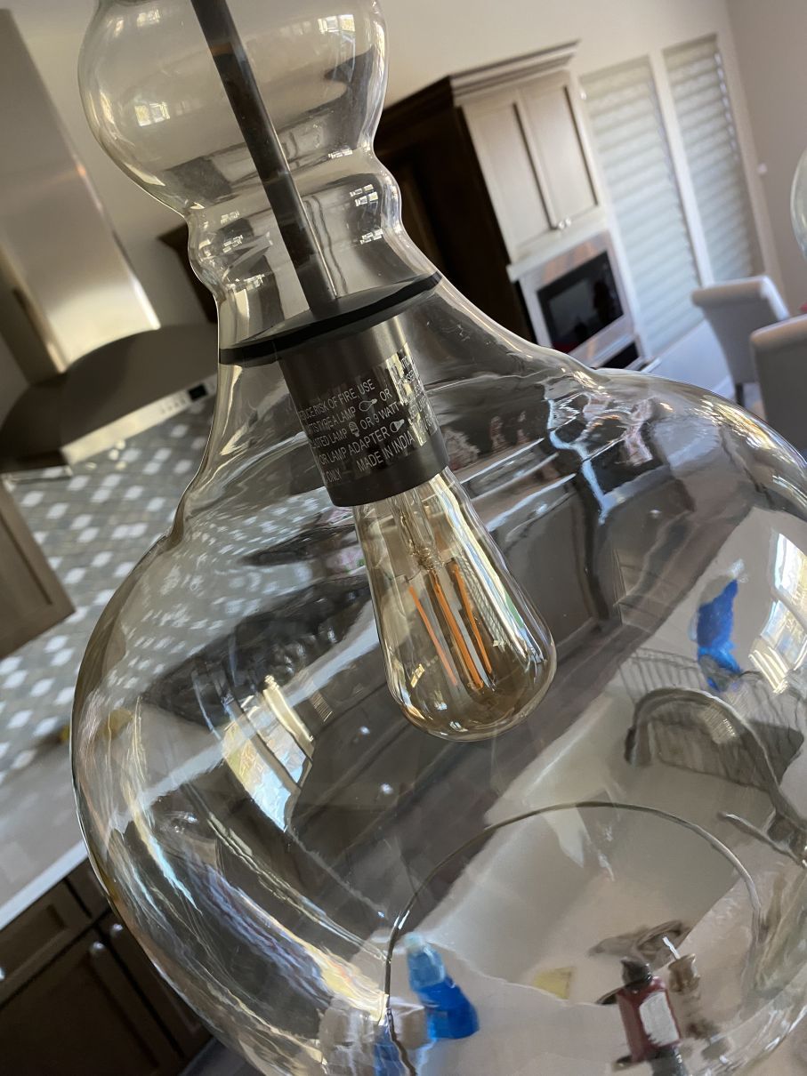 Close-up of a clear glass pendant light with a visible bulb in a modern room.