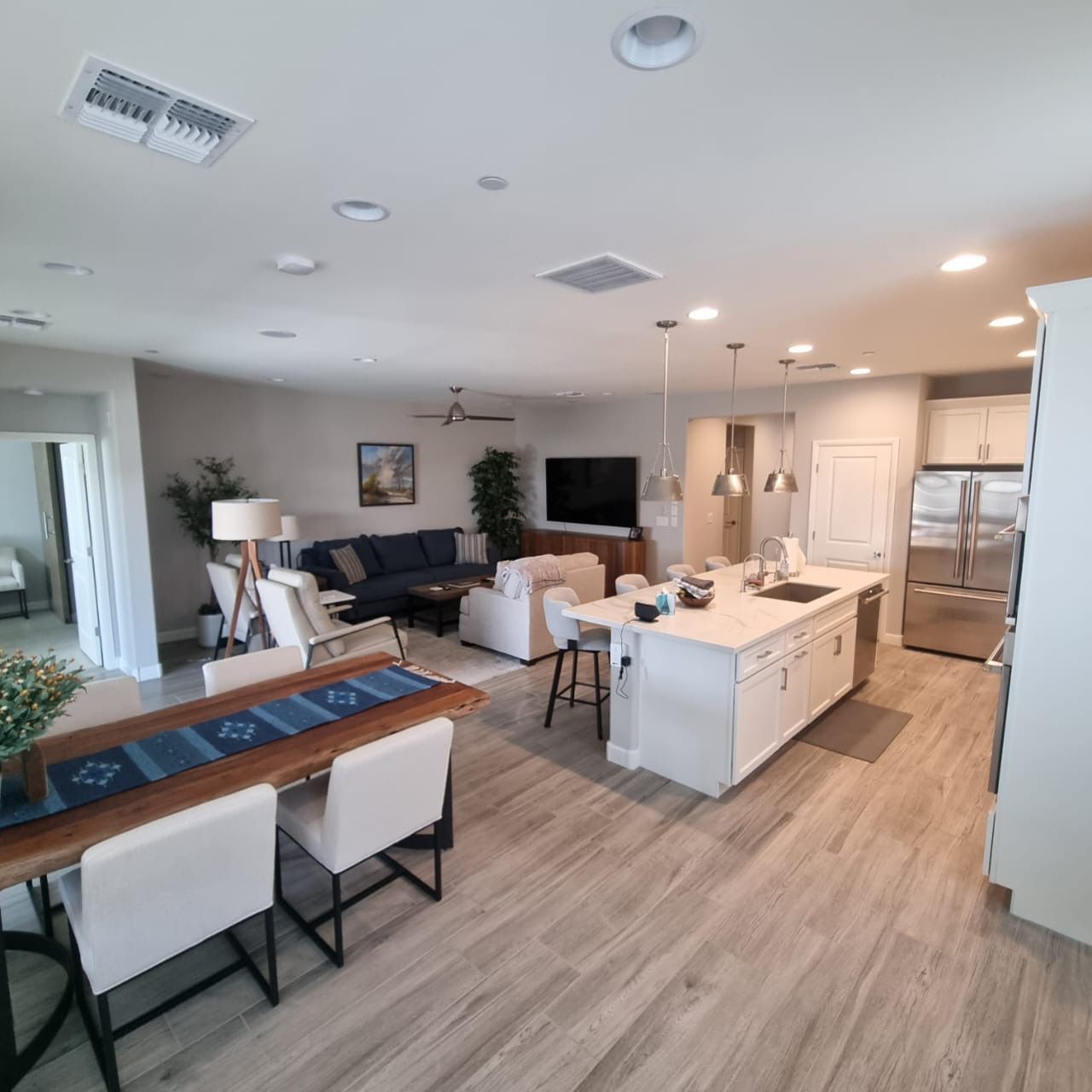 Open-plan living room and kitchen with white island, gray sofa, dining table, and wood-look flooring