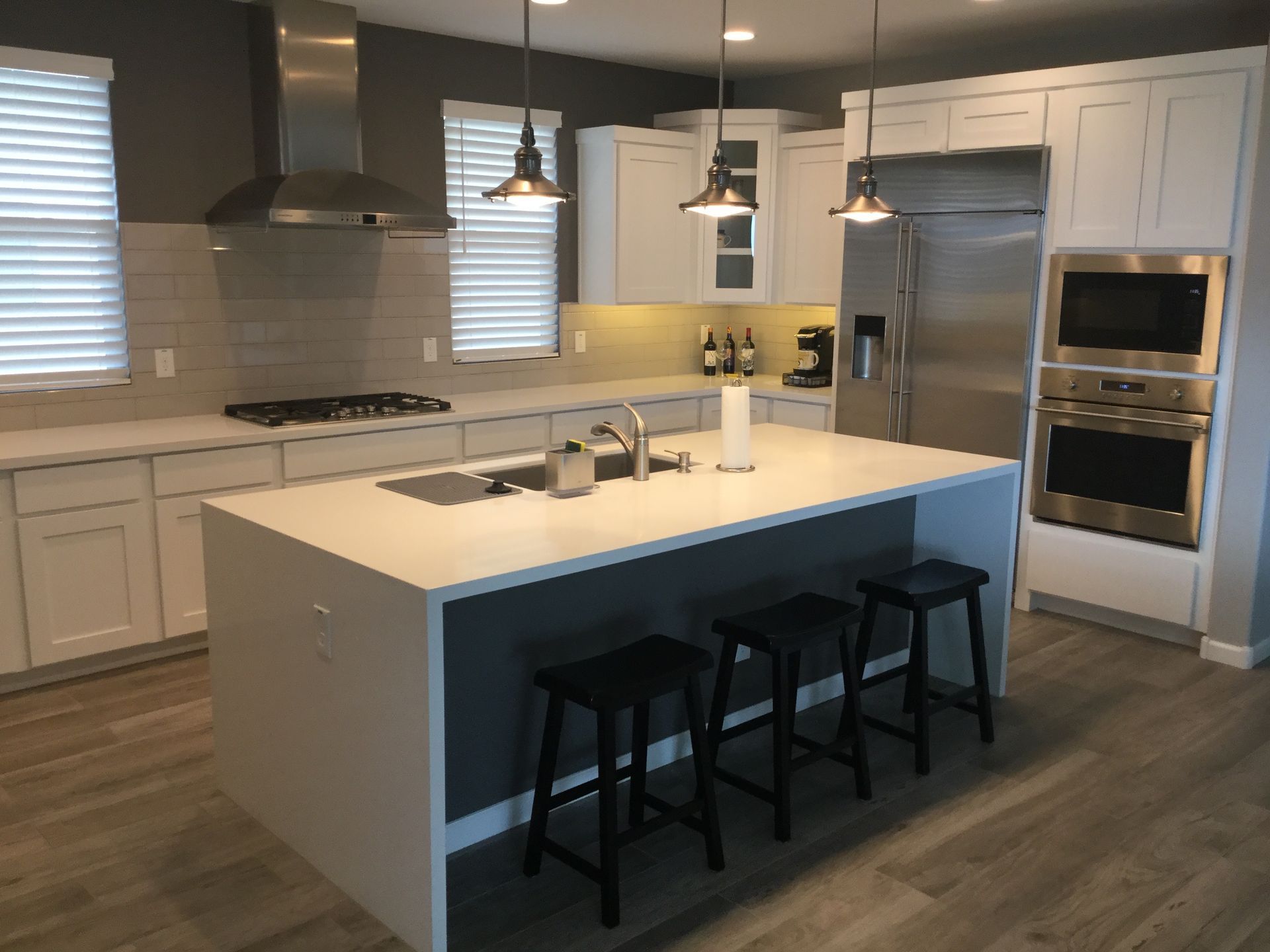 Modern white kitchen with island, black stools, pendant lights, and stainless steel appliances