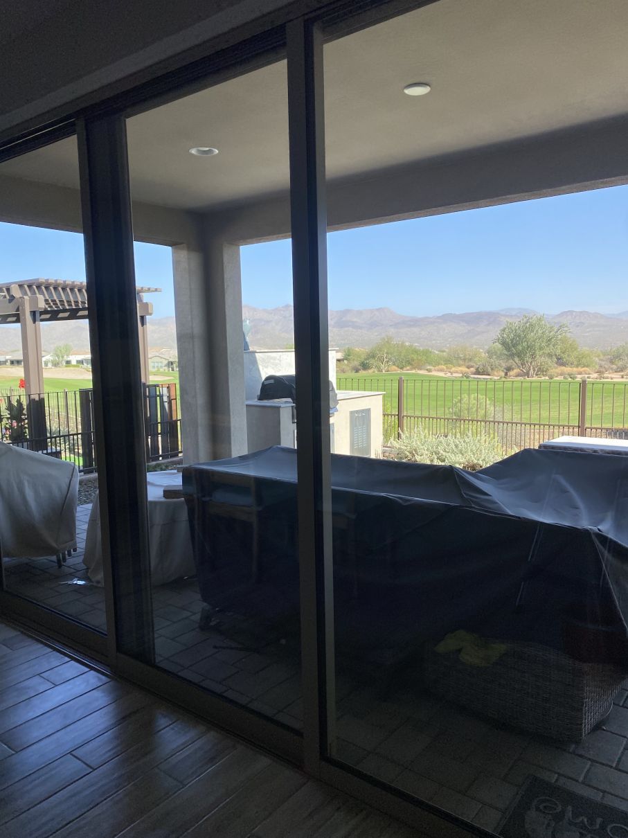 Covered patio with glass doors, outdoor furniture, and a view of green hills beyond a railing