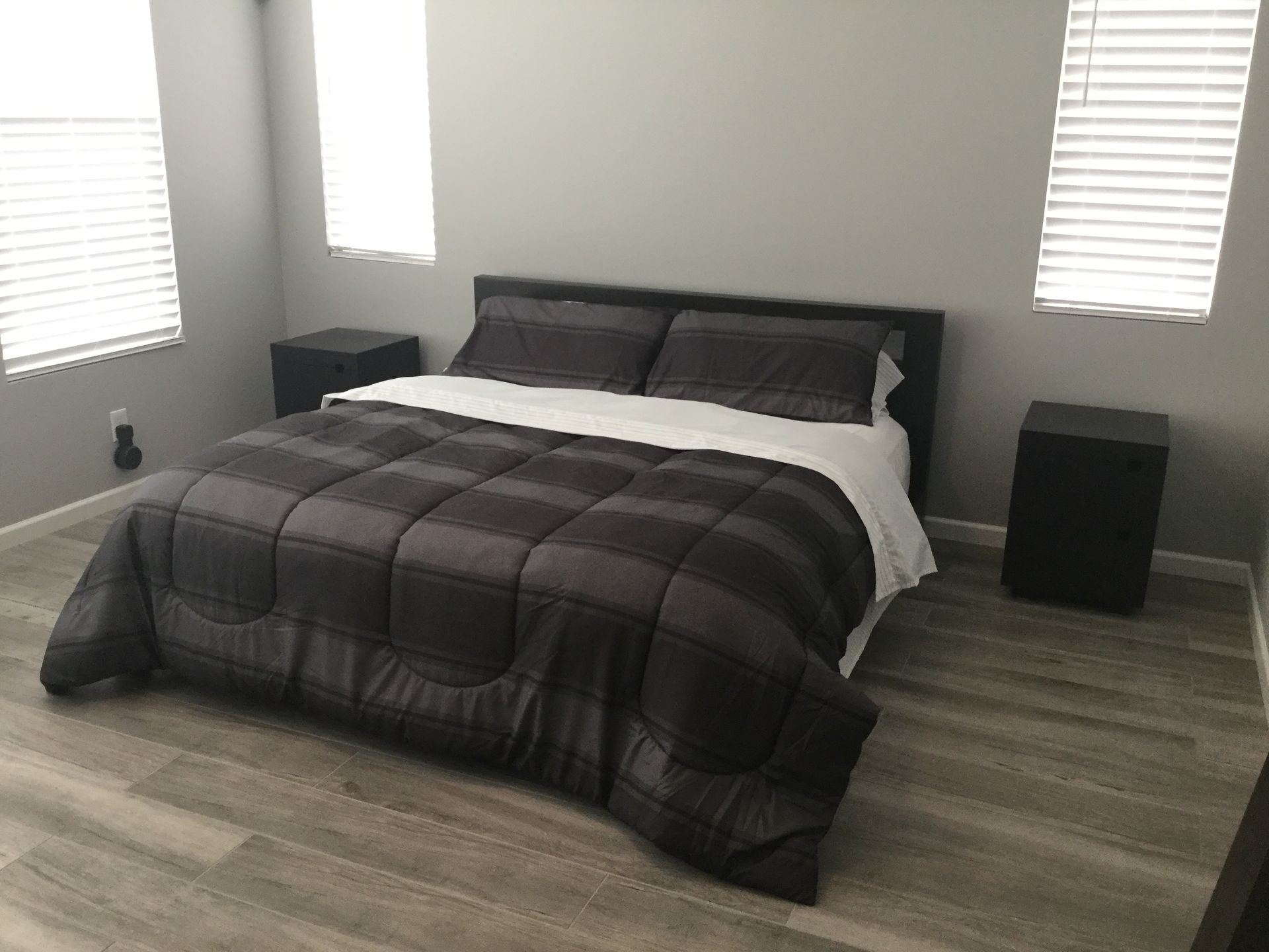 Minimal bedroom with a dark bed, gray bedding, and two windows with blinds