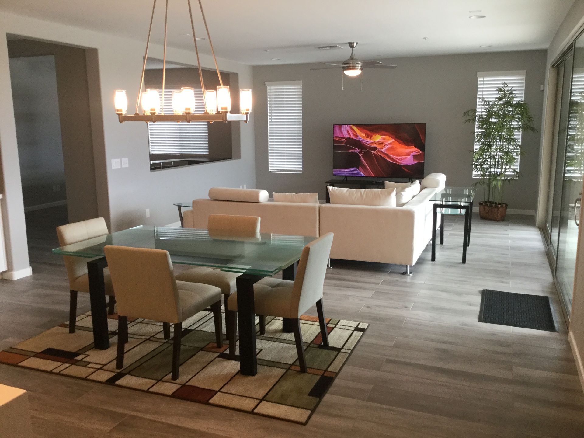 Modern open-concept living room and dining area with beige sofas, glass dining table, TV, and pendant lighting.