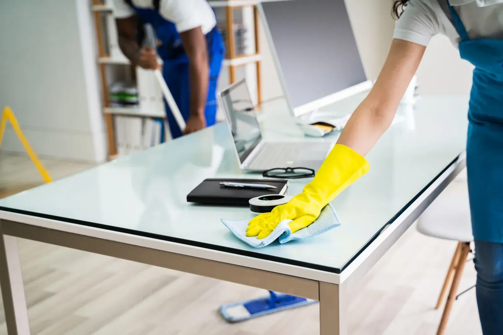Gloved cleaner wiping a glass table in a bright office setting
