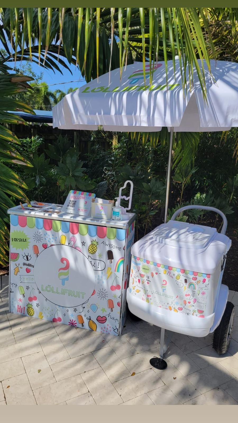 An ice cream cart is sitting next to a table with a white umbrella.