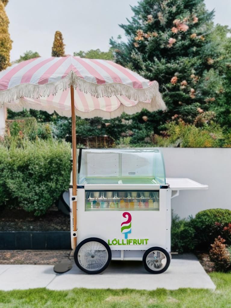 An ice cream cart with a pink and white striped umbrella.