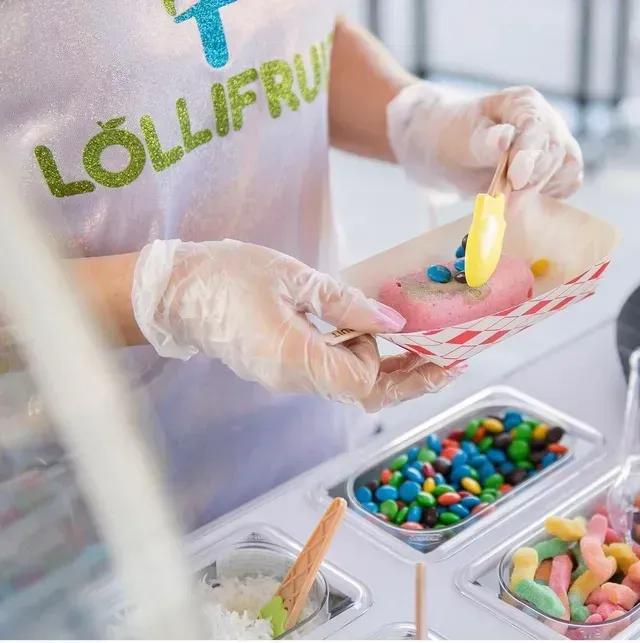 Gloved hands serving colorful candy into a paper tray at a sweet shop counter