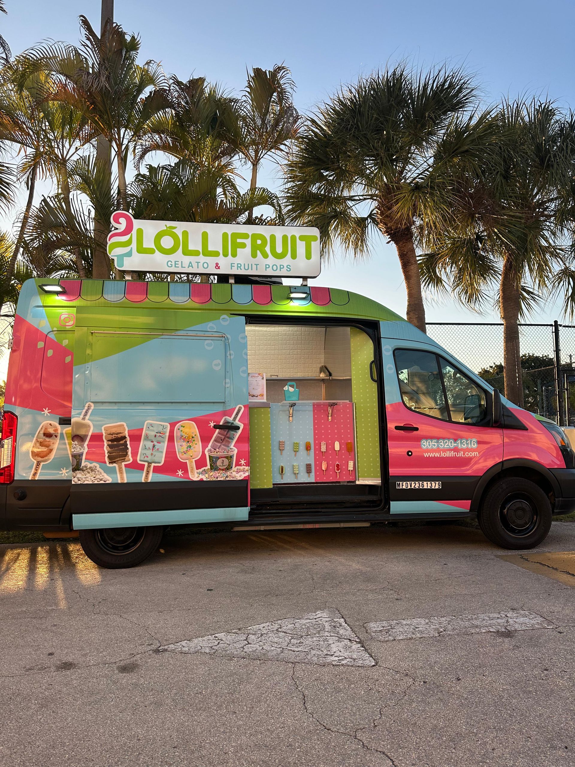Colorful Lollifruit ice cream truck parked outdoors by trees at sunset.