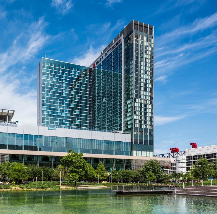 Modern glass hotel and tower beside a waterfront under a blue sky