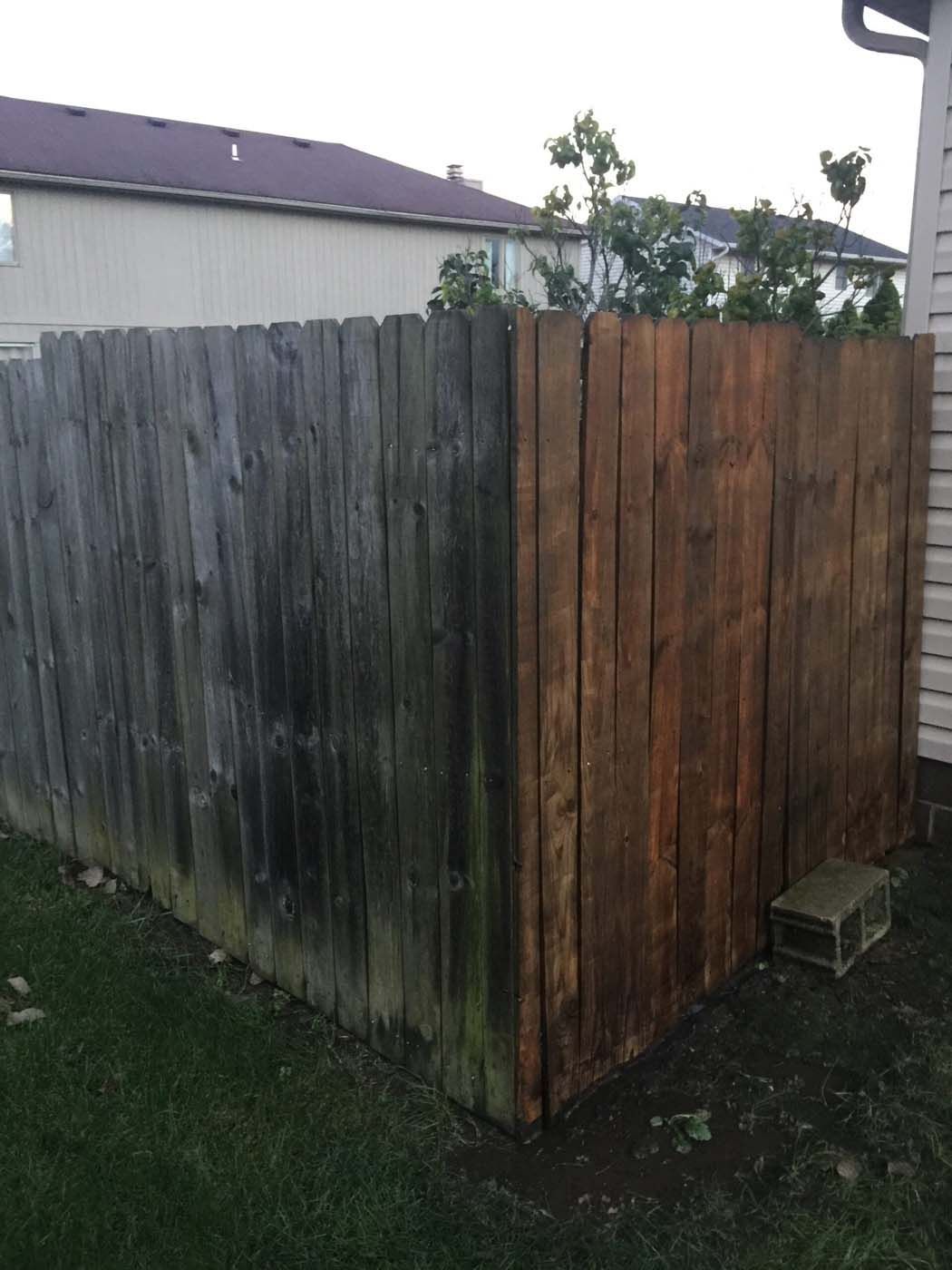 Wooden fence, half weathered and gray, half newly stained brown, in a backyard.