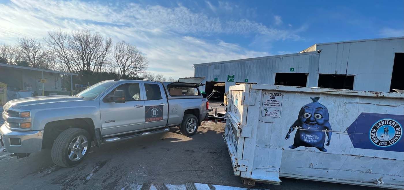Silver pickup truck next to a dumpster with a cartoon character, in front of a building.