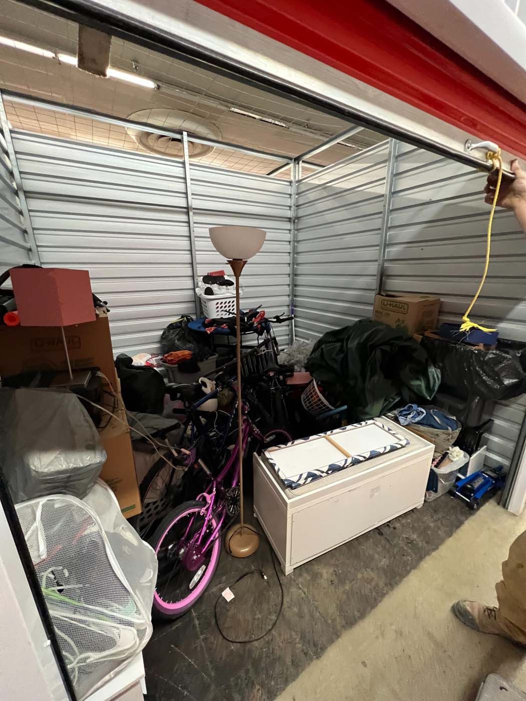 Storage unit with various items: bike, lamp, boxes, bags. Person pulling cord.