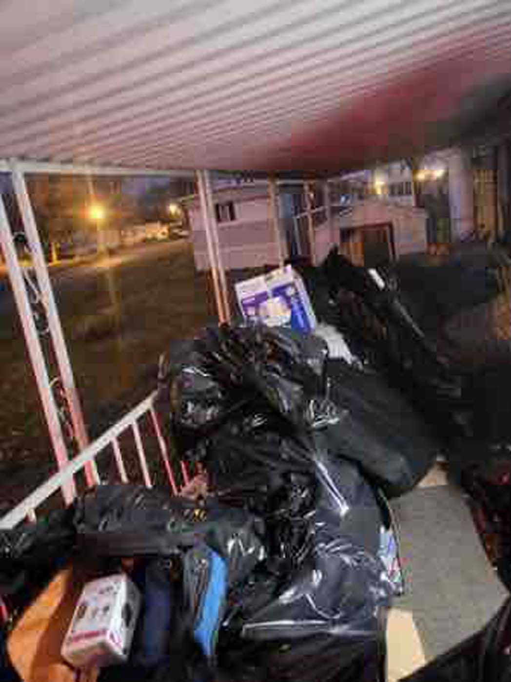 Black garbage bags and boxes piled on a porch, suggesting a move or cleanup. Outdoors at night.