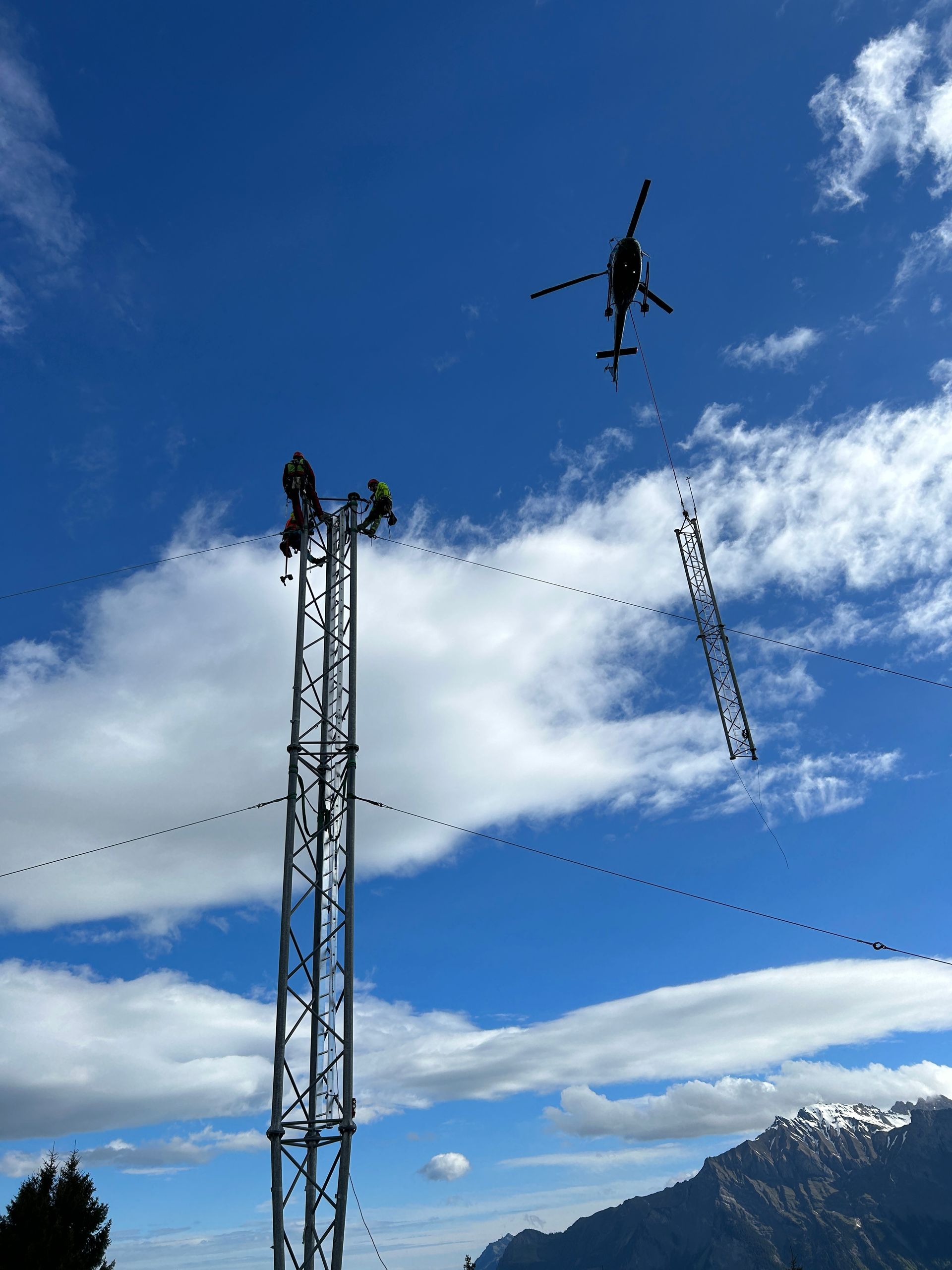 Ein Hubschrauber fliegt über einen Windmessmast mit einem Berg im Hintergrund.