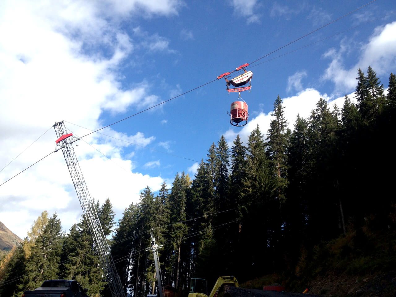 Eine Materialseilbahn fährt an einem sonnigen Tag über einem Wald.