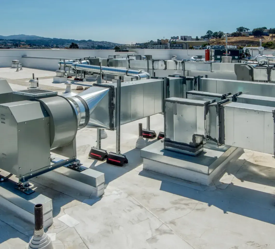 Rooftop HVAC system with metal ductwork and fans on a flat white roof against a clear blue sky.