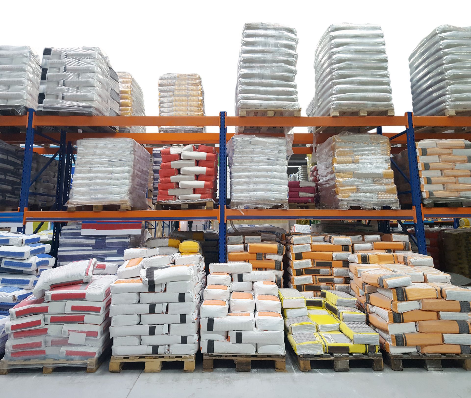 Scaffali di un magazzino pieni di pallet di prodotti insaccati, di vari colori, ben illuminati.