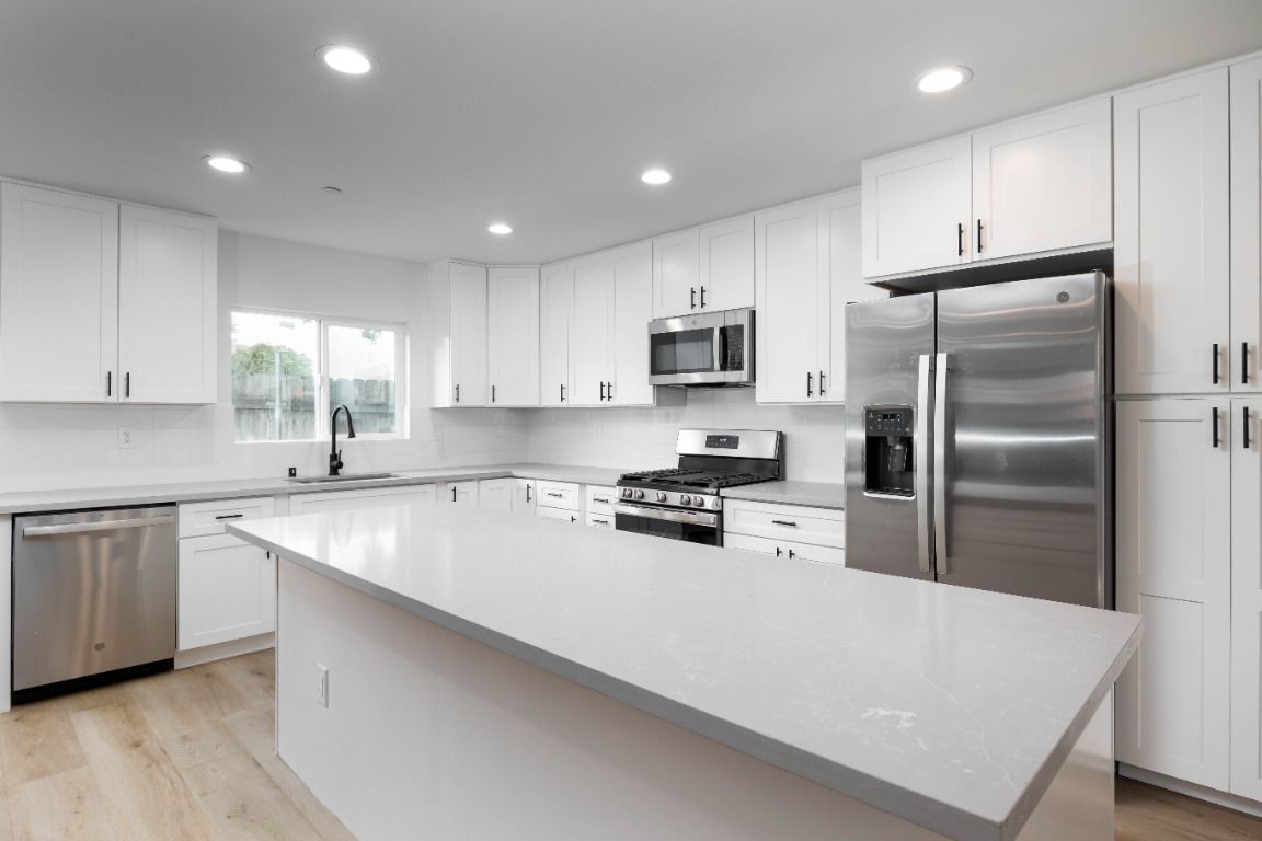 A kitchen with white cabinets , stainless steel appliances , and a large island.