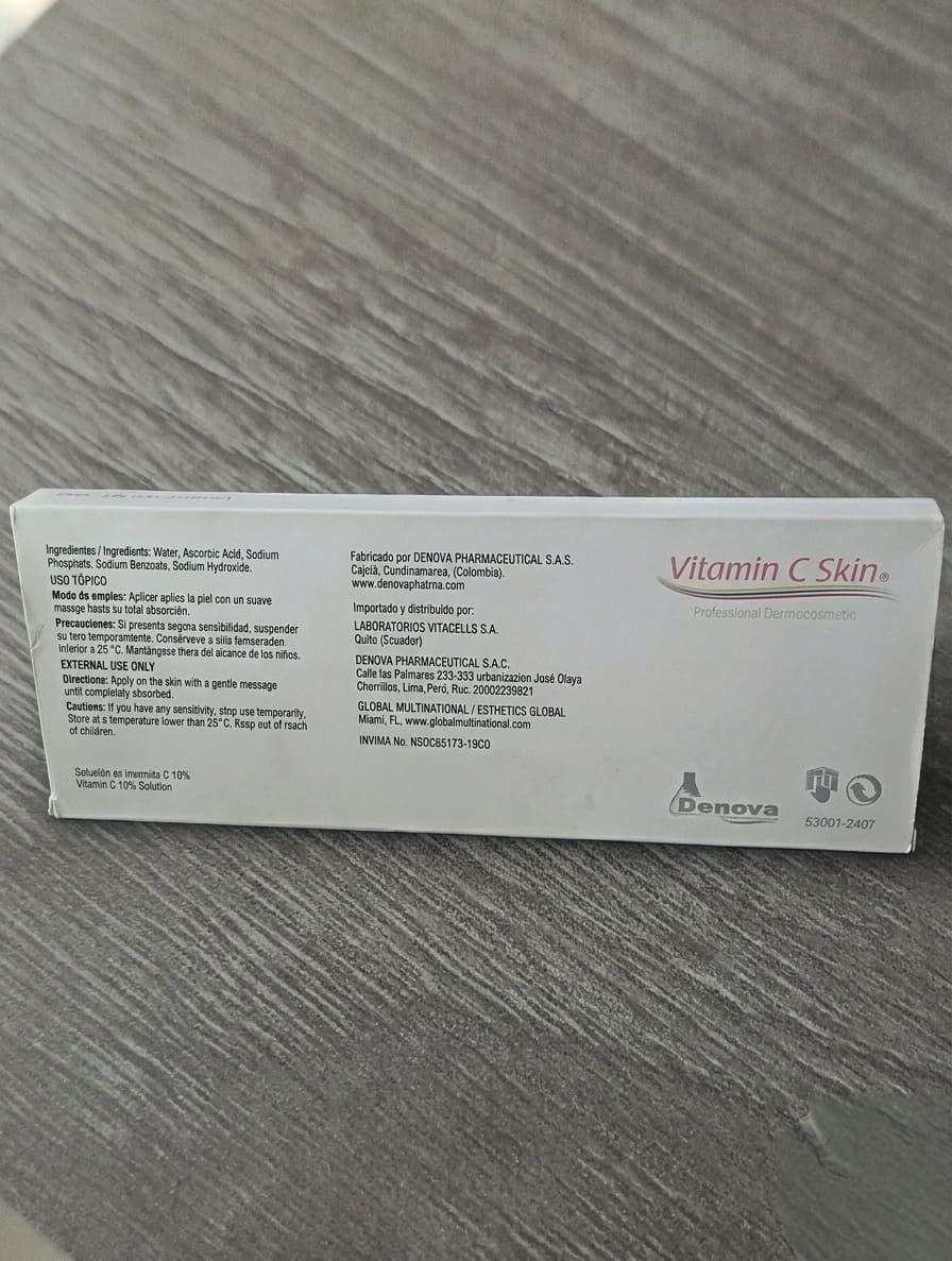 Caja blanca de producto para el cuidado de la piel con vitamina C sobre una superficie gris con texto rosa y negro.