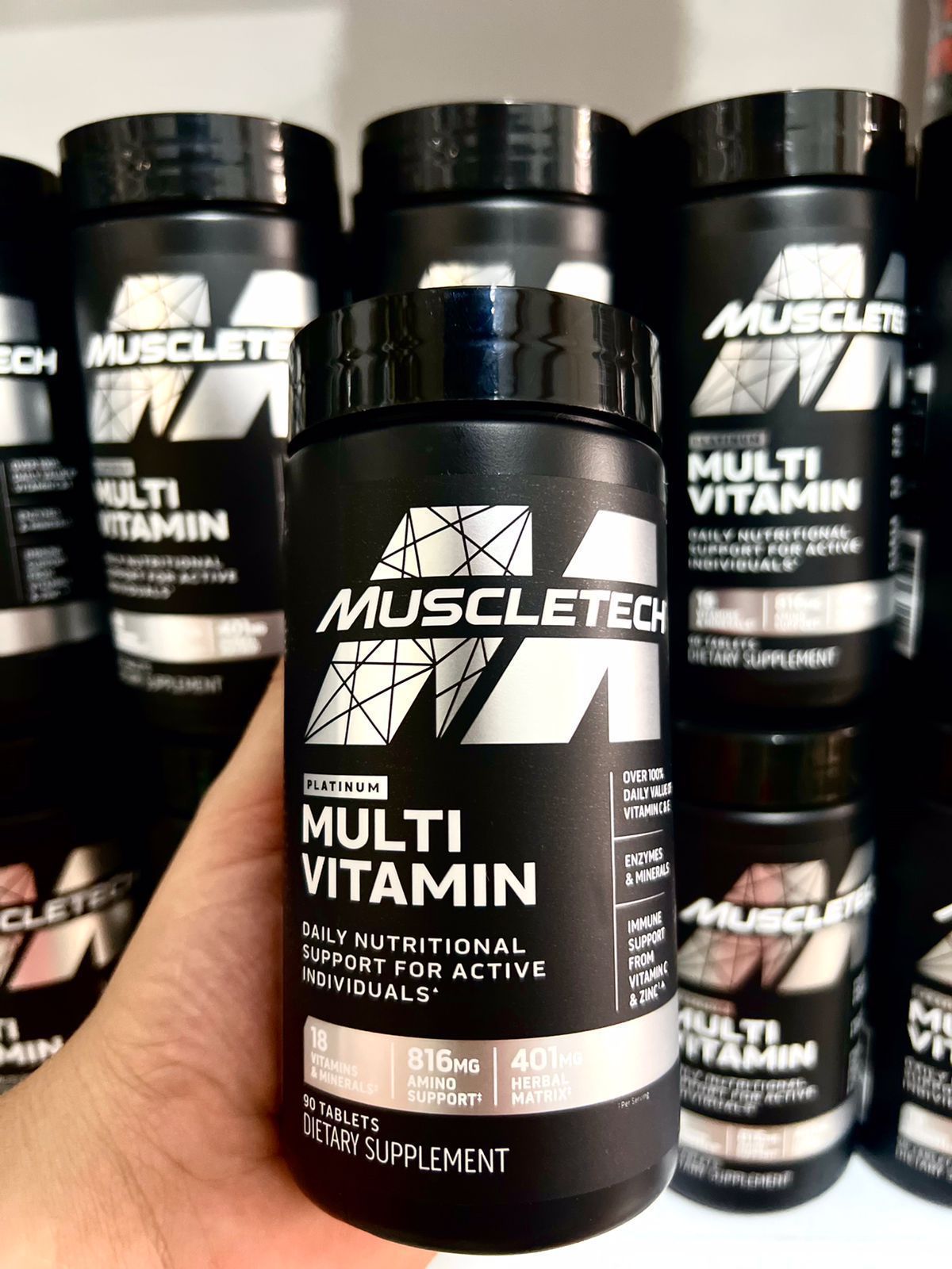 Frasco de suplemento multivitamínico MuscleTech negro con etiqueta blanca y plateada sobre fondo blanco.