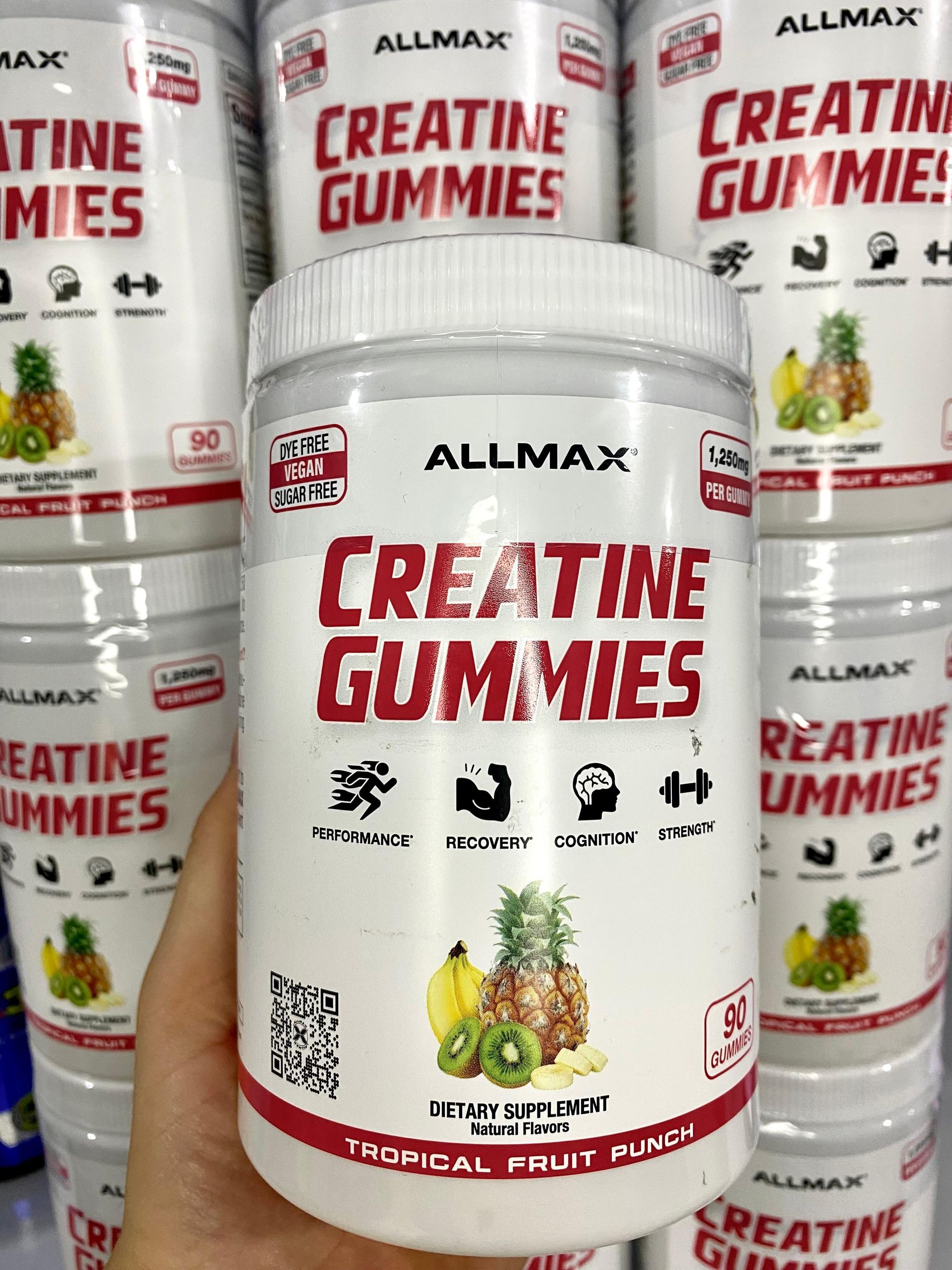 Envase de gomitas de creatina Allmax, tarrina blanca con texto rojo, sabor a ponche de frutas tropicales.