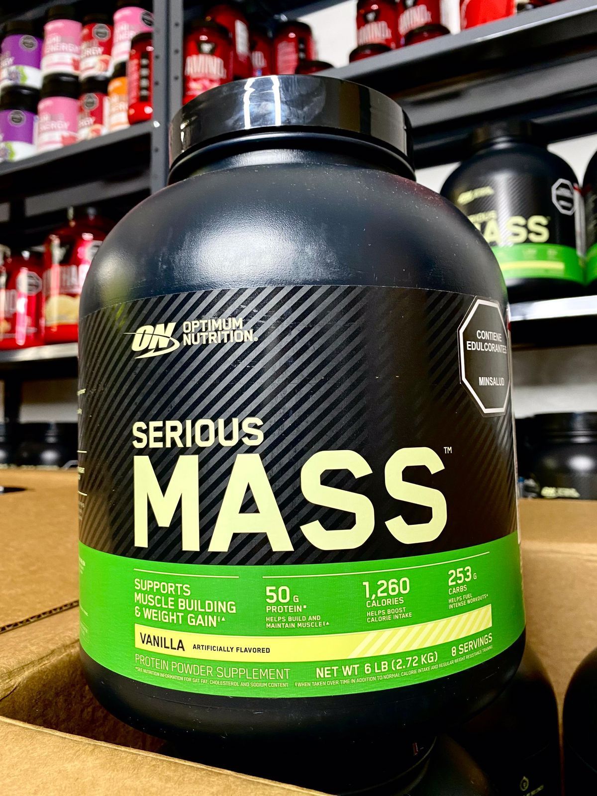 Frasco negro de suplemento proteico con la etiqueta “Serious Mass” y una banda verde sobre fondo oscuro.