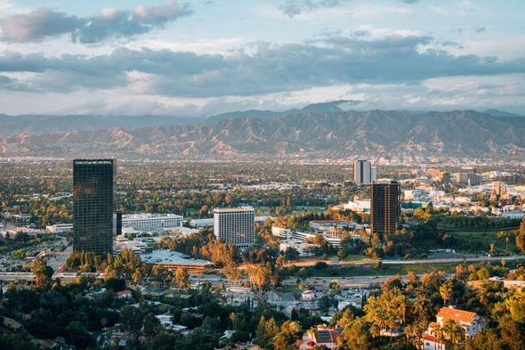 Wide cityscape with tall buildings, distant mountains, and a cloudy sky at sunset Wide cityscape with tall buildings, distant mountains, and a cloudy sky at sunset