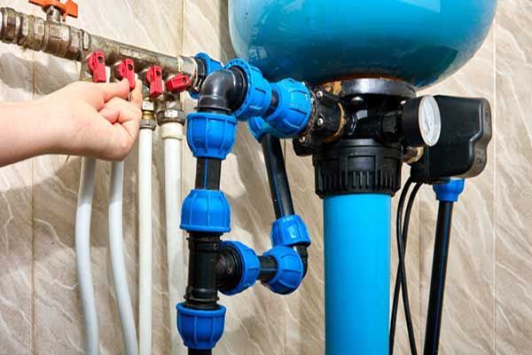 Hand adjusting blue and black water filtration pipes and valves under a sink