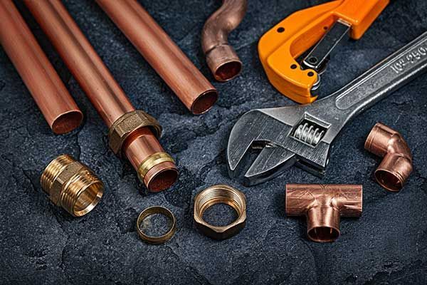 Copper pipes, fittings, and a wrench on a dark work surface with an orange pipe cutter Copper pipes, fittings, and a wrench on a dark work surface with an orange pipe cutter