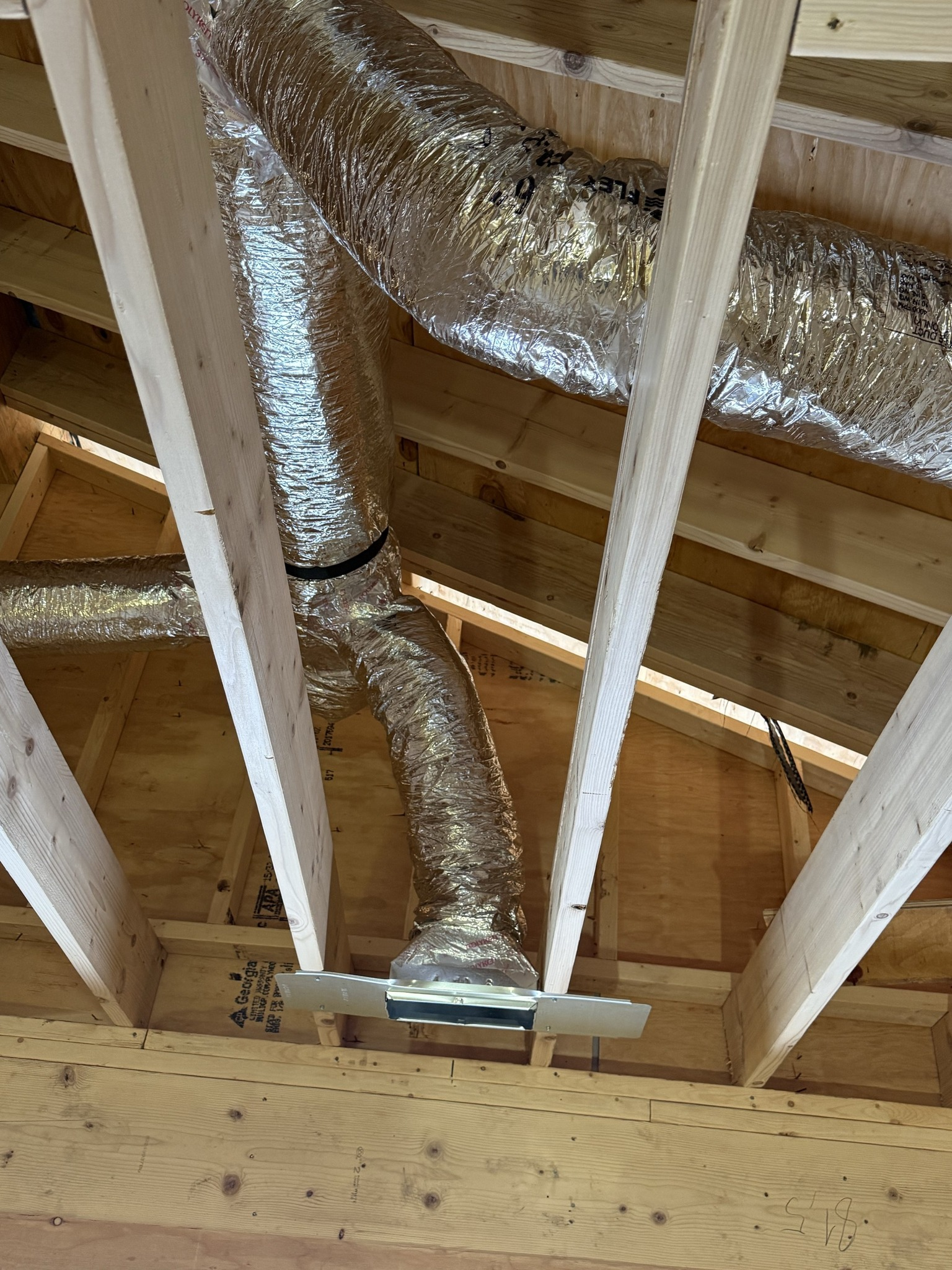 Foil-insulated HVAC ductwork running through exposed wooden ceiling joists