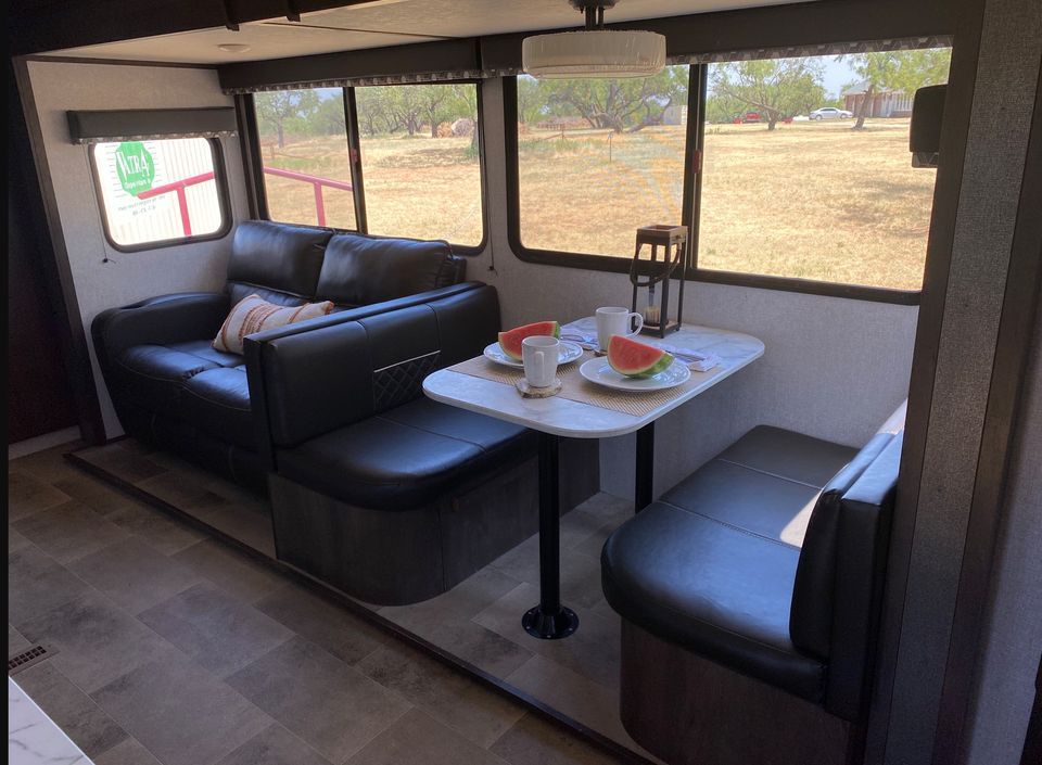 Cozy interior of a camper with a black sofa, table set for two, and large windows.