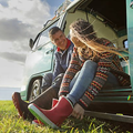 A man and woman sit on grass by a vintage van, enjoying a relaxed conversation.