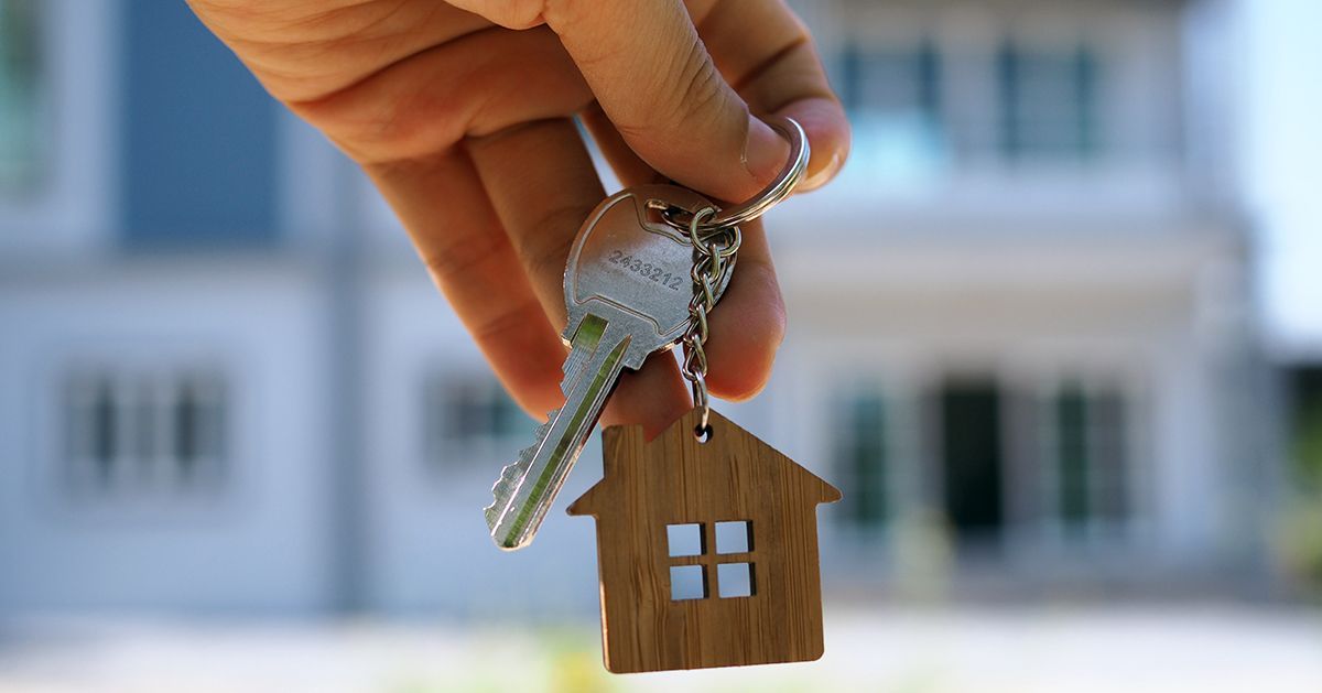 Eine Person hält ein Schlüsselpaar mit einem Hausschlüsselbund vor einem Haus.