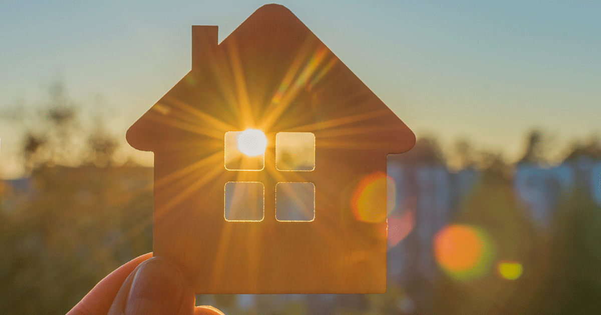 Eine Person hält ein Modellhaus in der Hand, durch dessen Fenster die Sonne scheint.