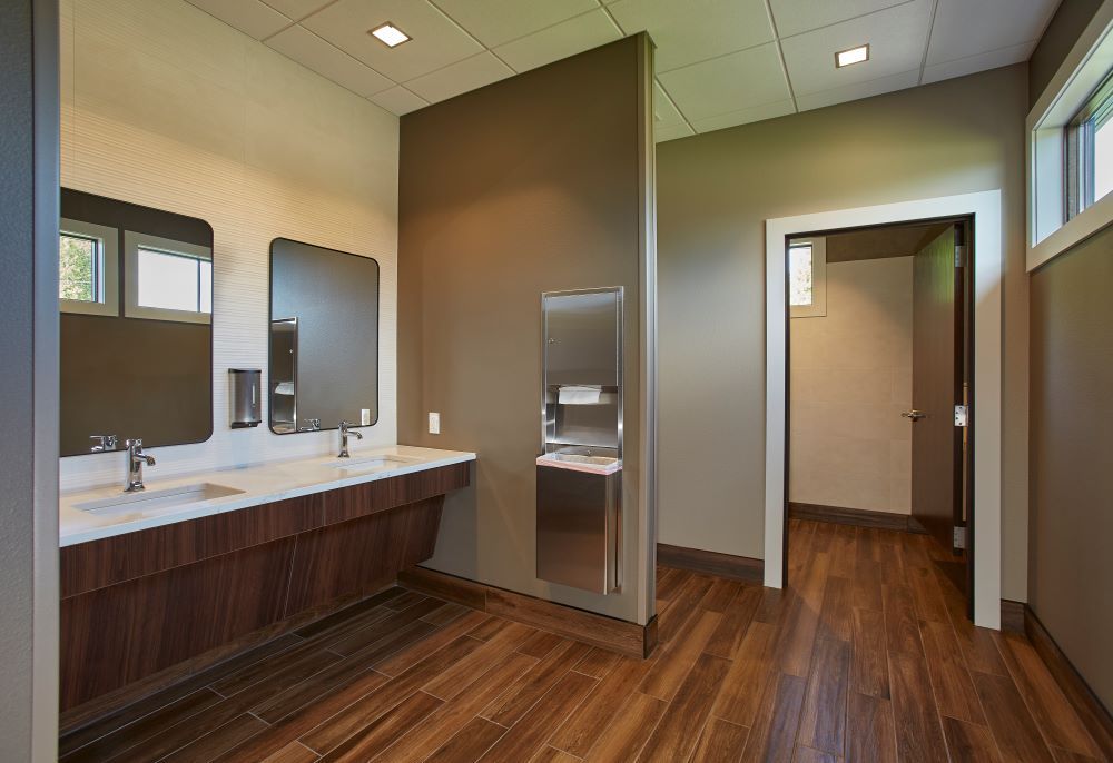 A bathroom with two sinks , two mirrors , and hardwood floors.