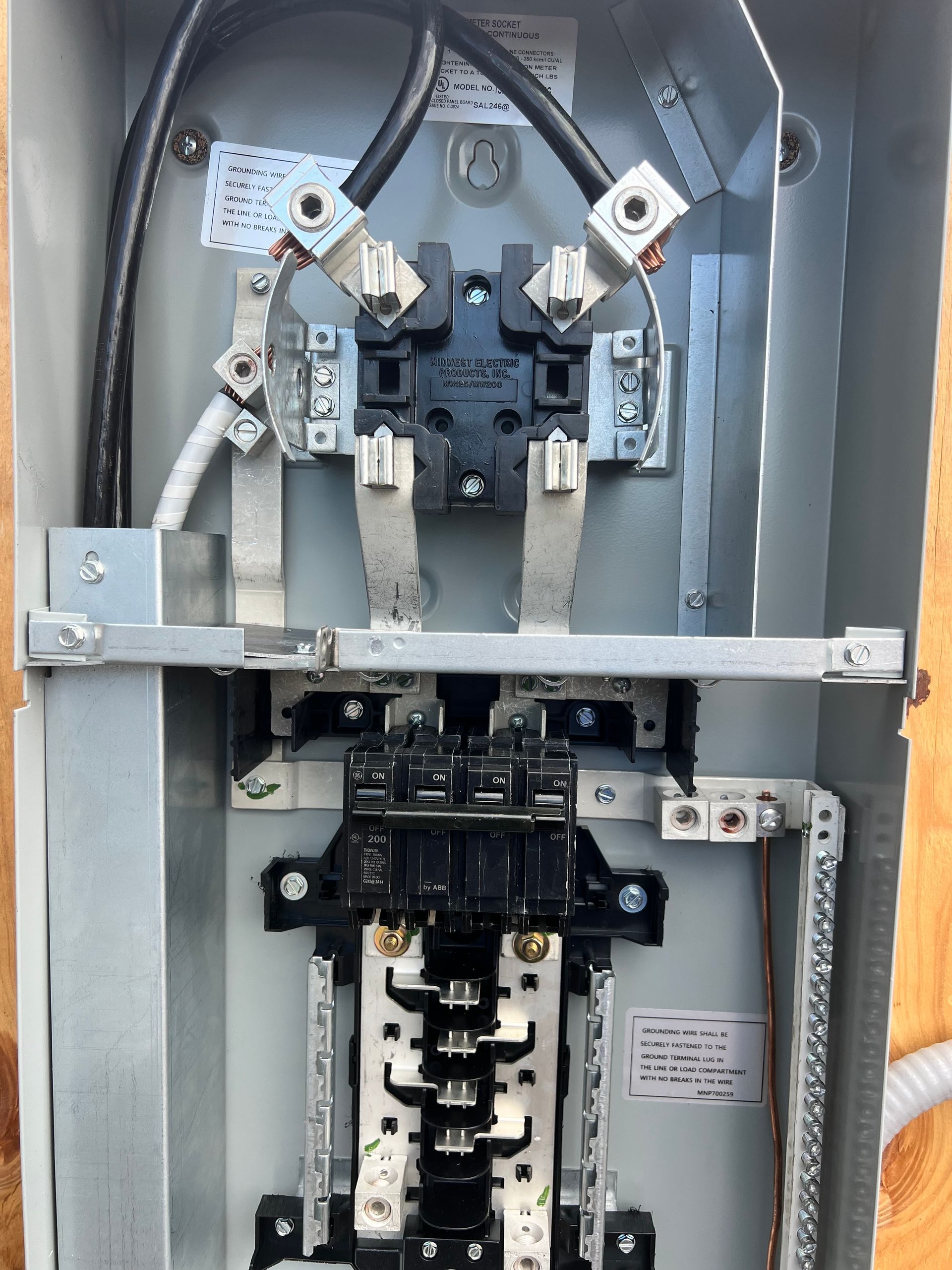 Electrician in overalls and cap working on a breaker panel.
