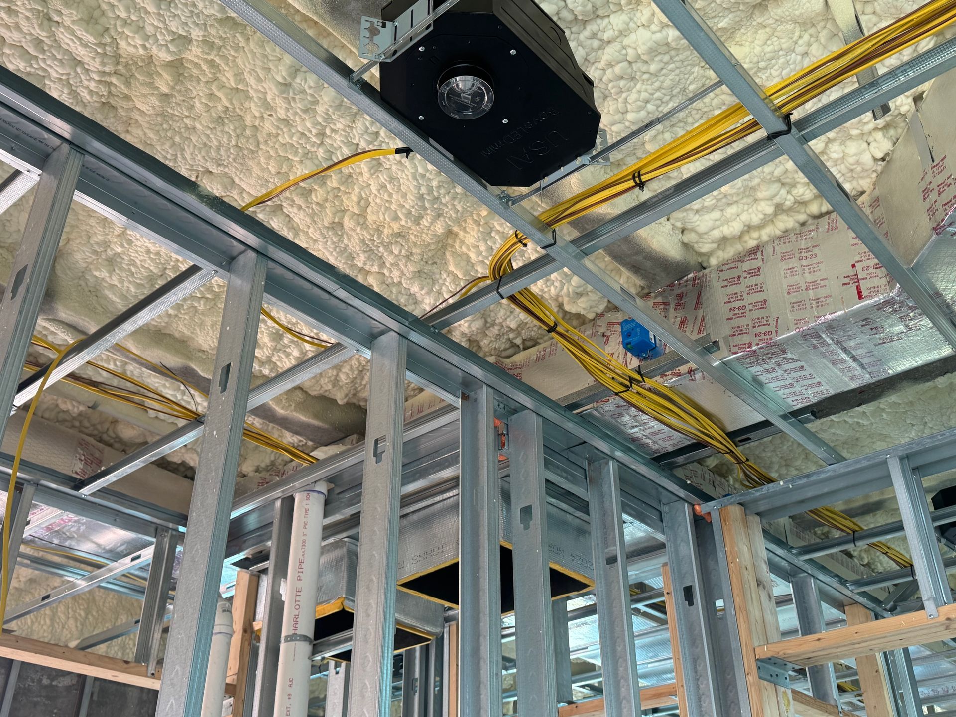 Electrician in a yellow hard hat working on an electrical panel in a building.