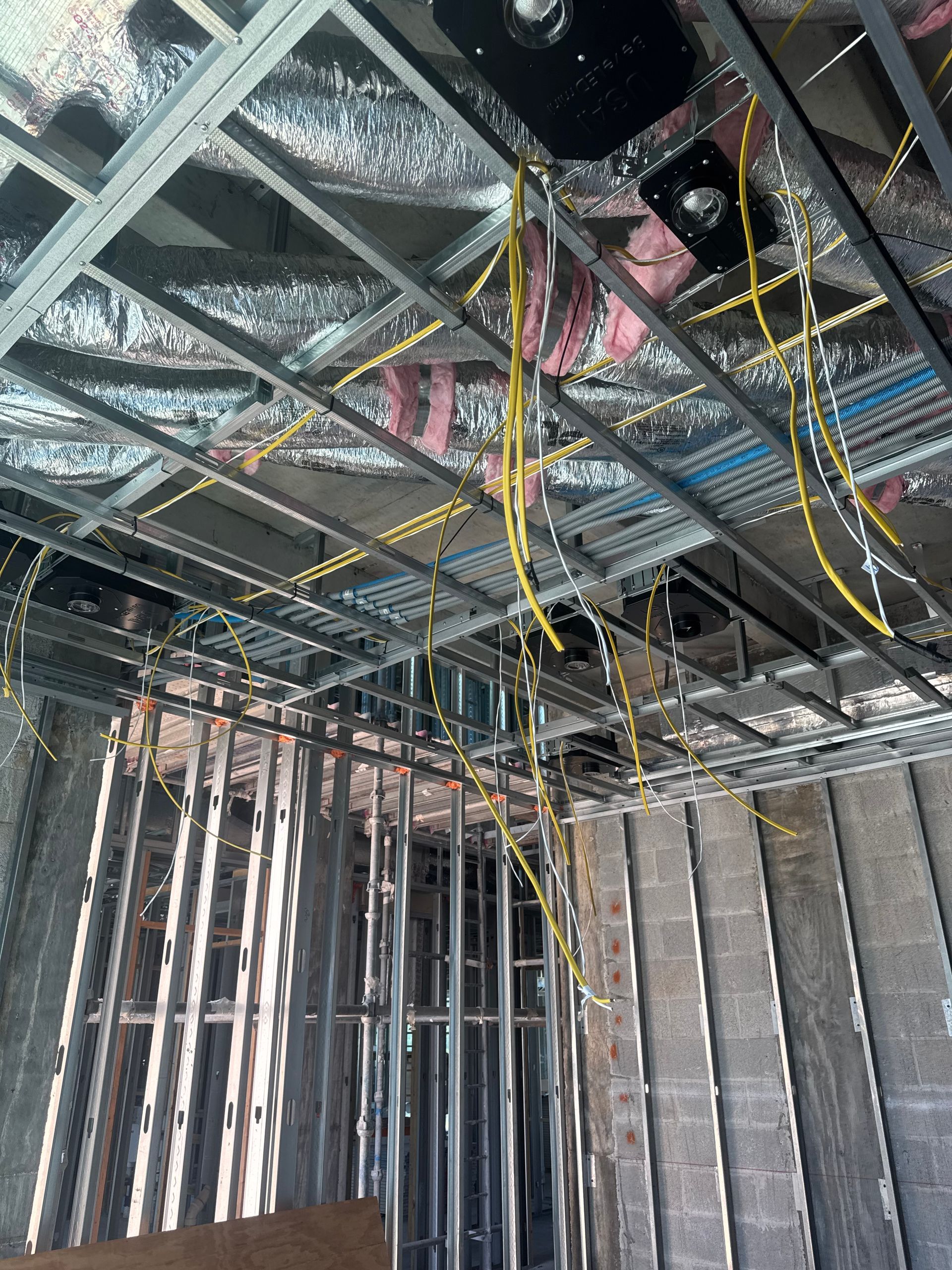 Construction site interior with exposed metal framing, wiring, and insulation.