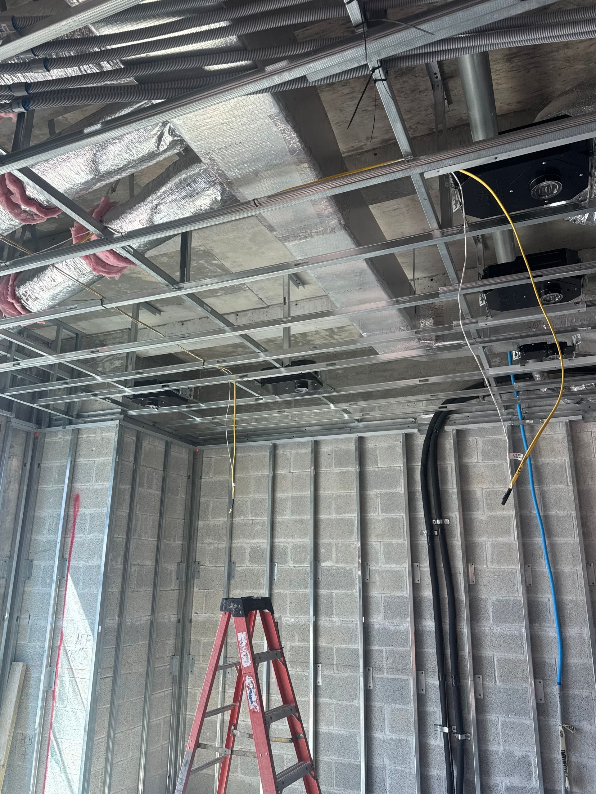 Construction site interior with exposed ceiling grid, concrete block walls, and a ladder.