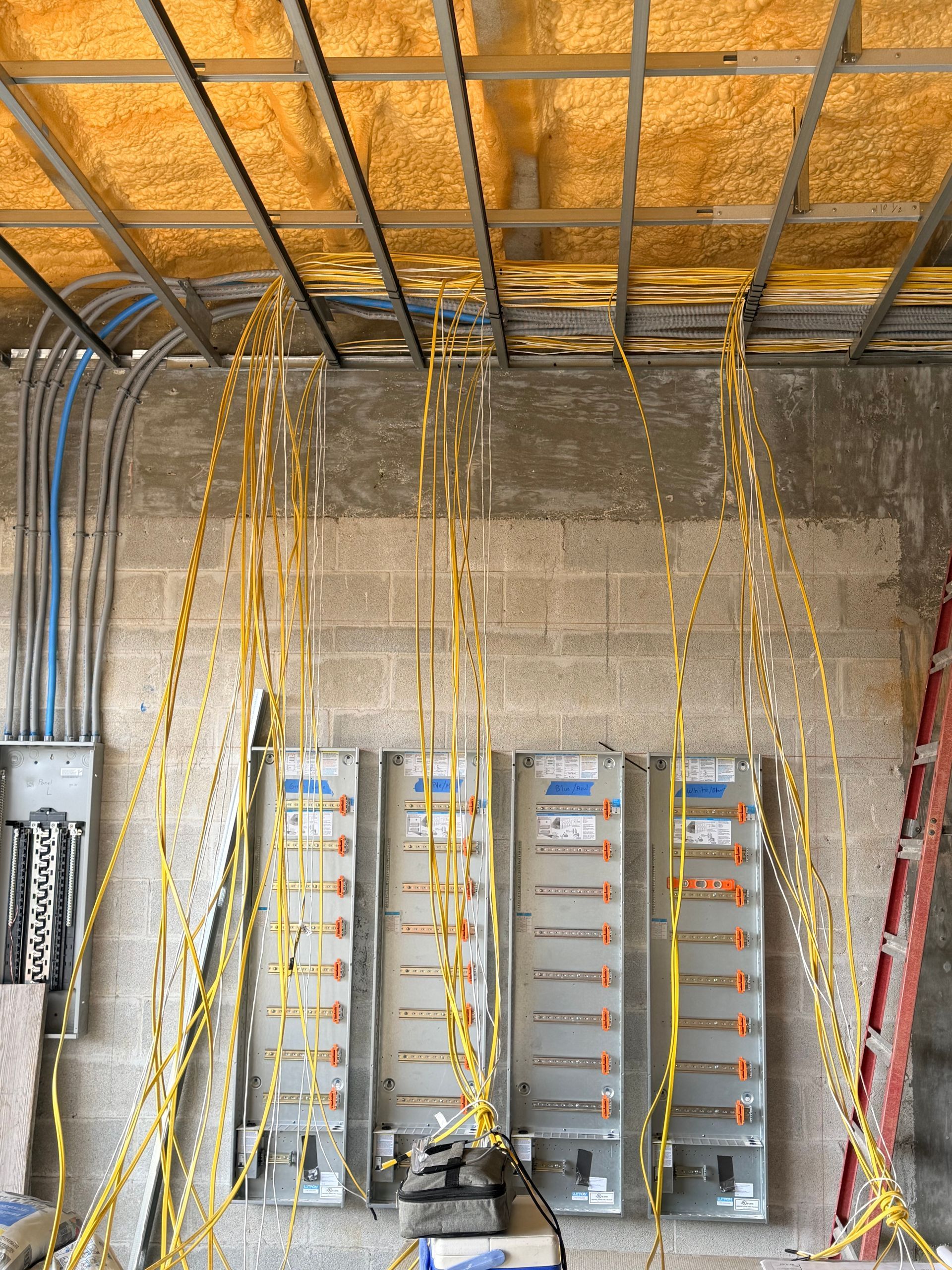 Electrical wiring installation: yellow wires hanging from ceiling to electrical panels on a concrete wall.