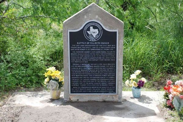 Memorial plaque on a stone marker surrounded by flowers in a wooded area Memorial plaque on a stone marker surrounded by flowers in a wooded area